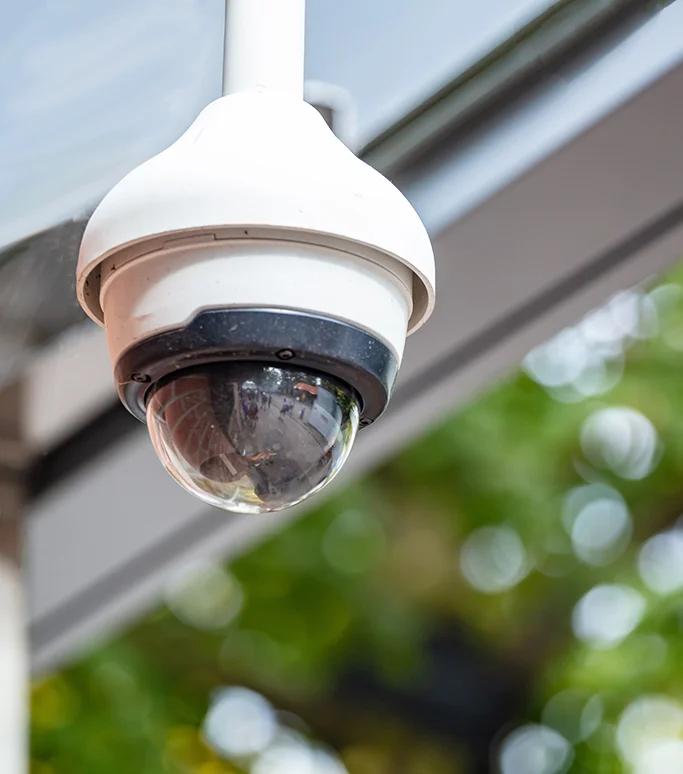 A close up of a CCTV camera with trees blurred in the background.