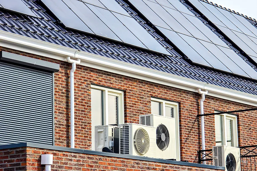 Renewable Energy for Homes Air source heat pump unit installed outdoors at a modern home with solar panels on the roof.