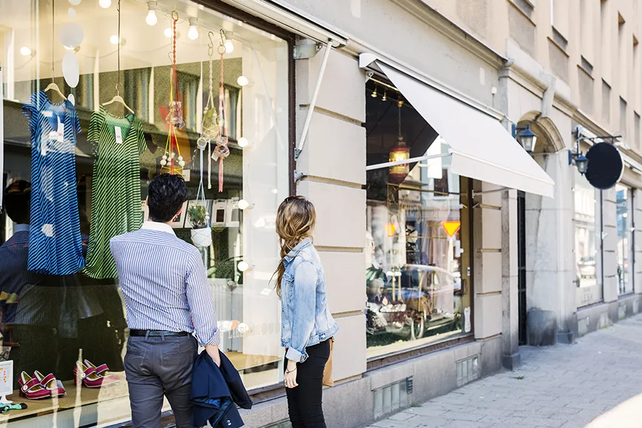 Couple looking at clothes displayed in a store shop window on a high street.