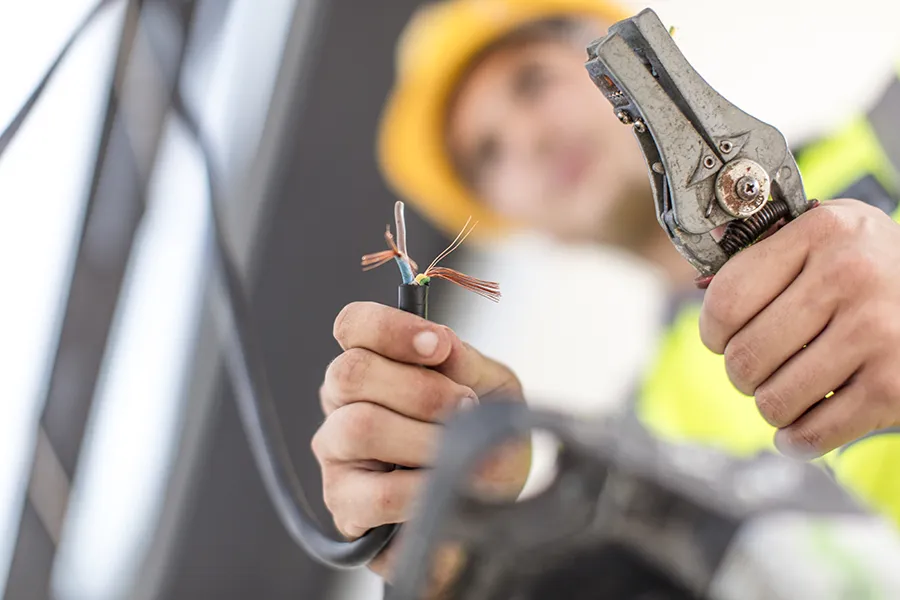 A close-up of an electrician holding a pair of wire cutters in one hand and a cable in the other.