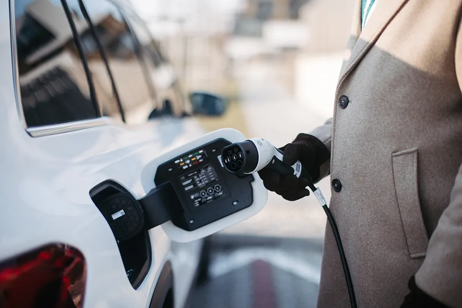 Close up of man wearing a long coat charging electric car.