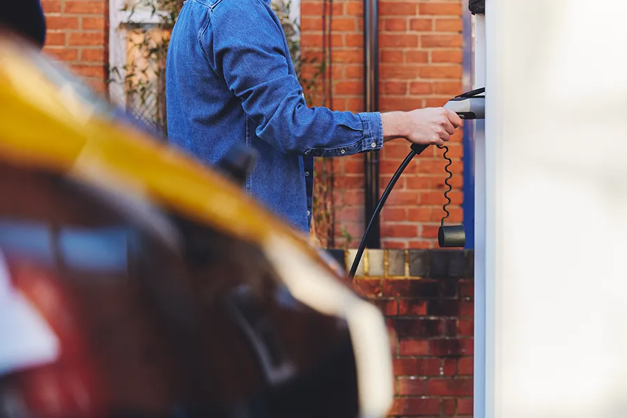 EV Charger Installation - A man plugging in electric car to charging point outside his home.