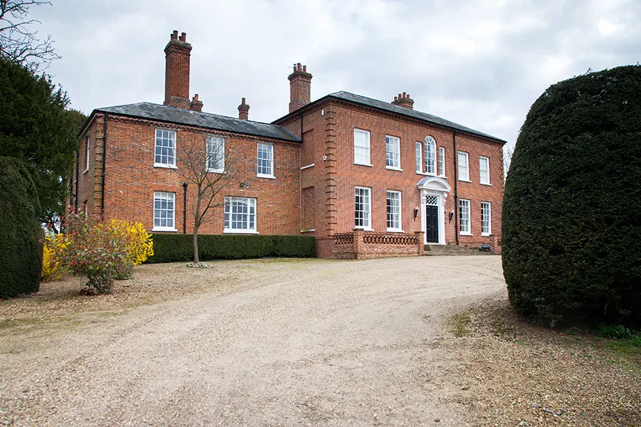 A large brick estate house with sash windows, tall chimneys and driveway.