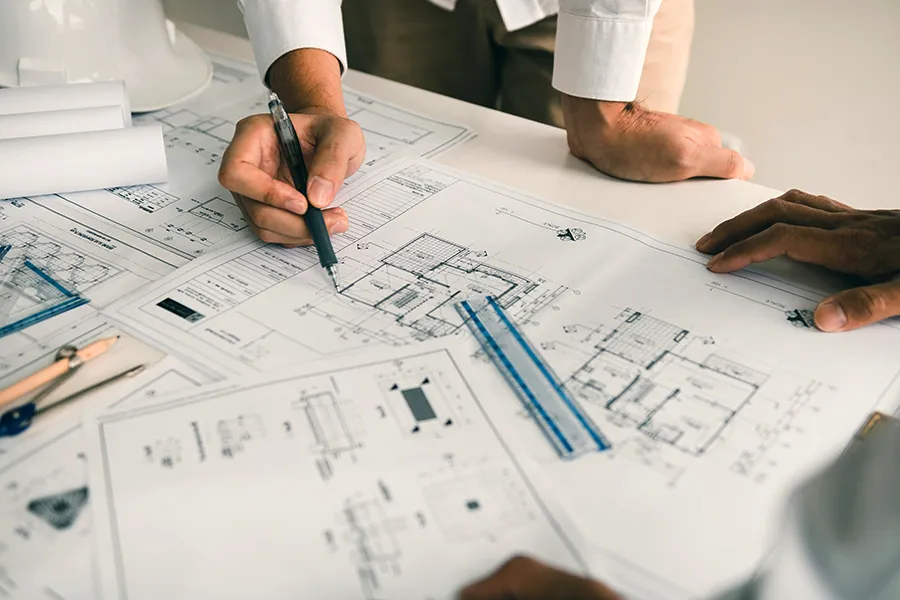 An electrician discussing electrical design with an architect whilst looking at plans on a table.