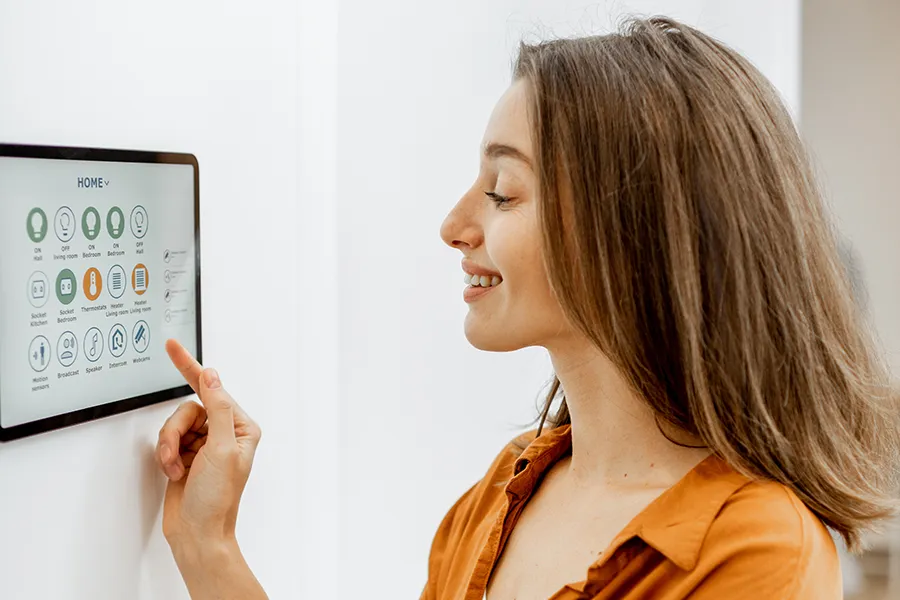 A woman controlling smart devices around the home with a digital tablet that is installed on a wall.