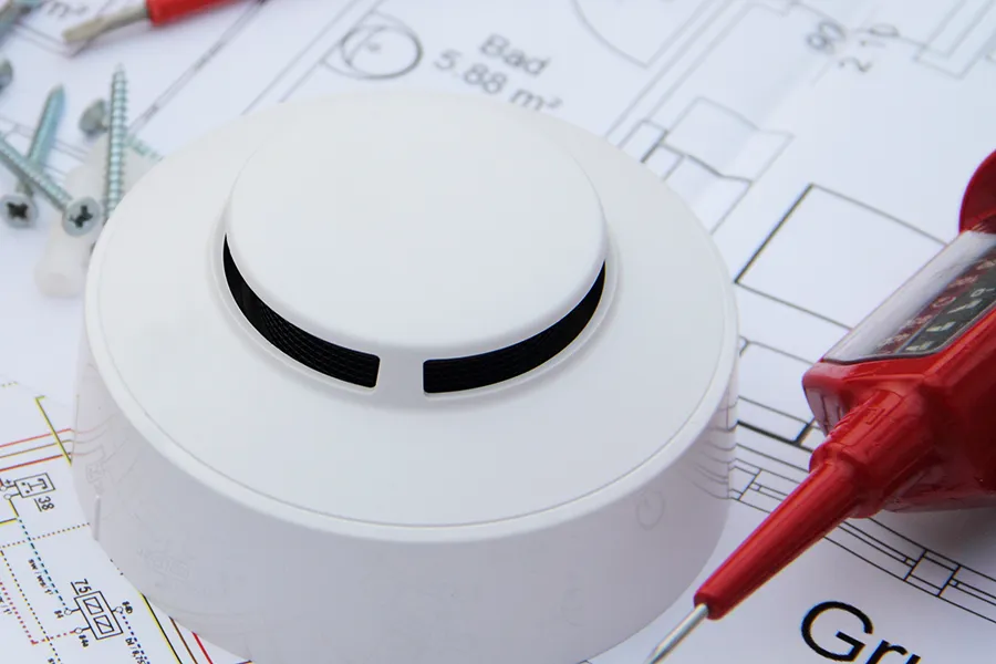 A smoke detector with an electricians screwdriver on a circuit diagram.