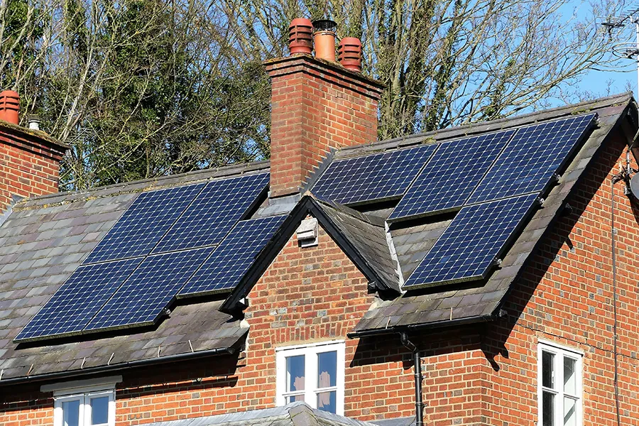 The Benefits of a Solar Panel Installation A solar panel installation on a brick house with a pitched slate rooftop in bright sunshine.