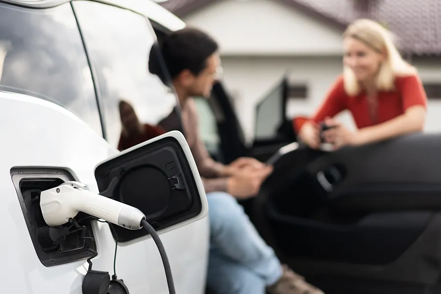 Couple having a conversation near charging electric vehicle outside a modern home.