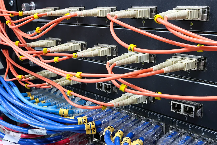 Data cabling terminating at the back of an office server, where labelled orange and blue network cables are plugged in.